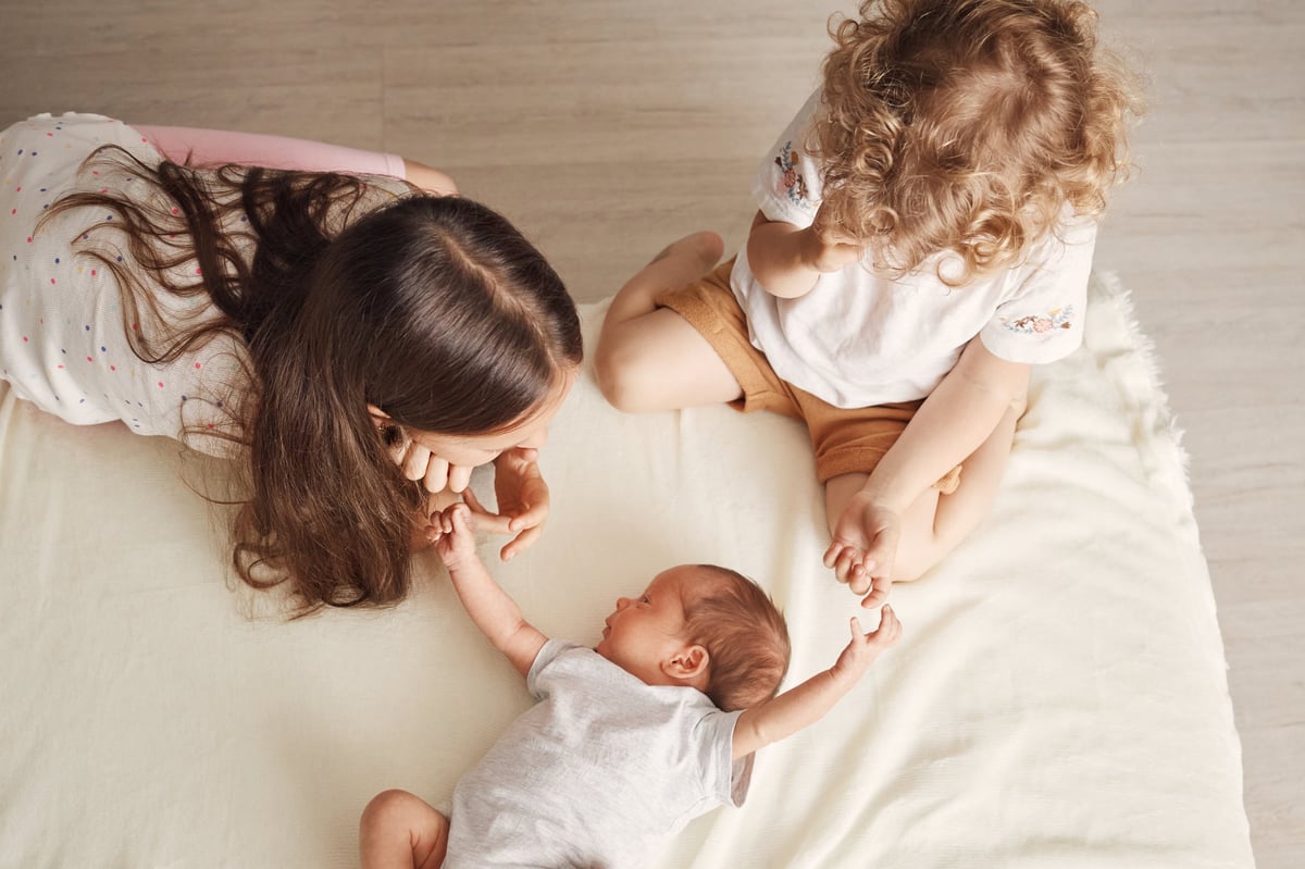 Sisters wearing T-shirts carefully cuddling their little brother whispering softly to him