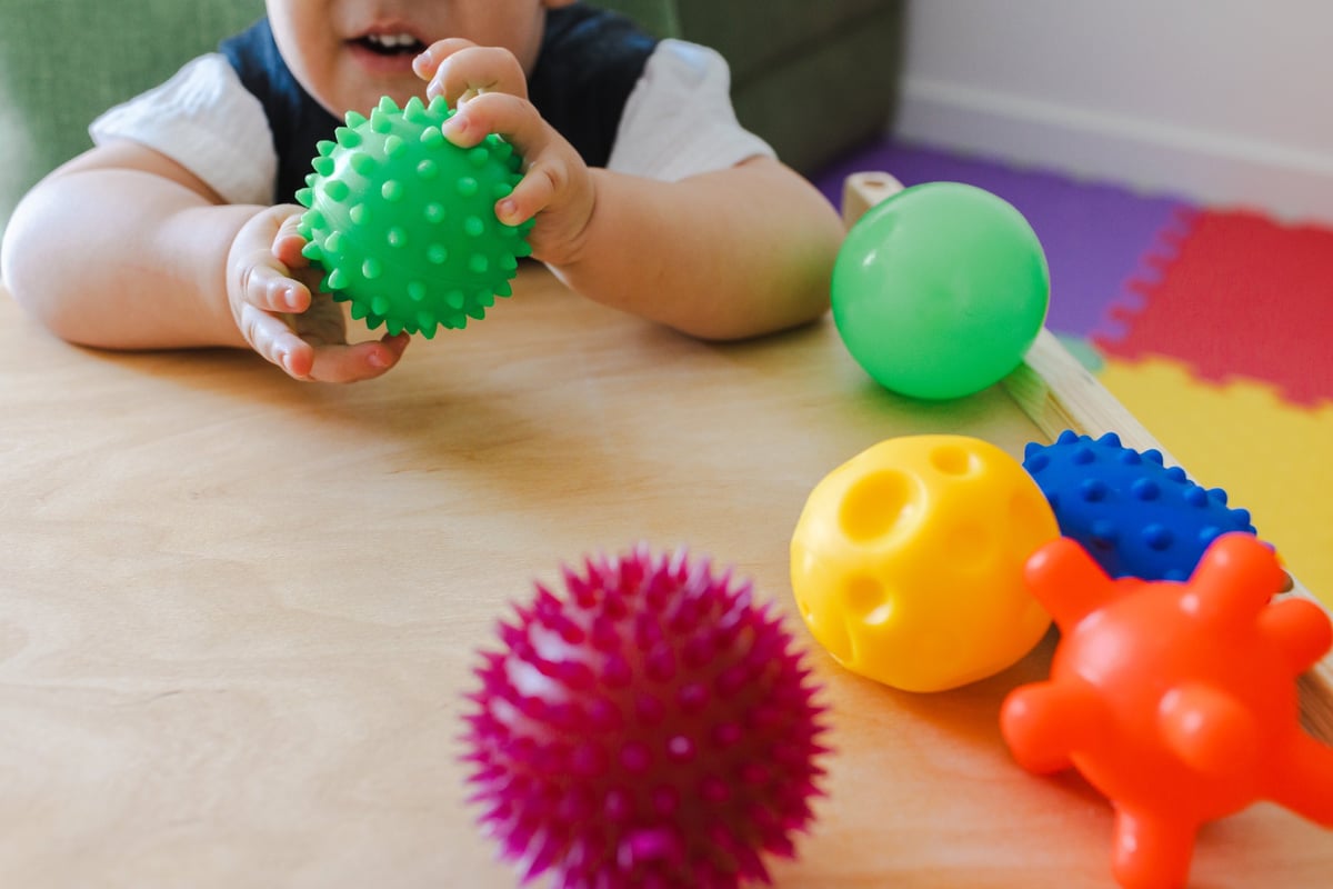 Little boy with coordination disorders participates in rehabilitation exercises, focusing on grip strength with various colorful soft balls while sensory integration therapy