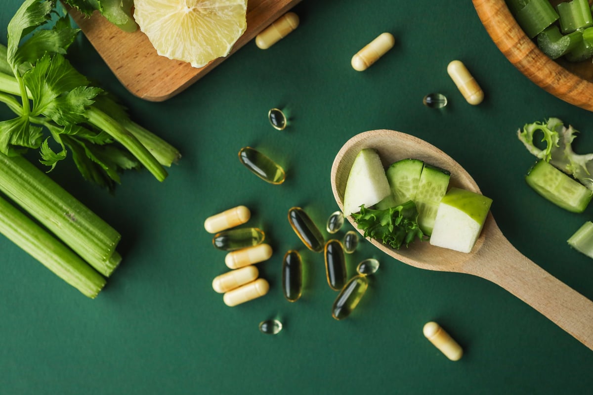 Chopped vegetables and vitamin capsules on wooden board